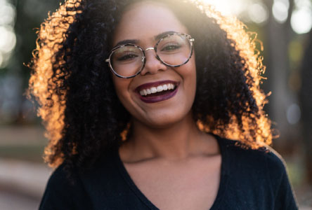 Young woman with curly hair and large glasses smiling at the camera.