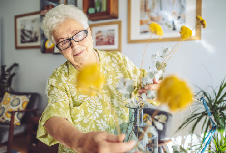 Elderly woman arranging yellow flowers in a vase.