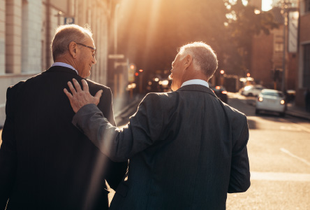 Two older businessmen walking down a street with their backs towards the camera.