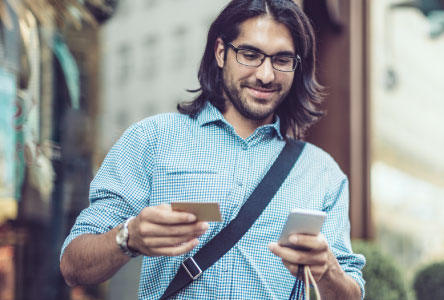 Man with long hair looking down at a smartphone and credit card he is holding.